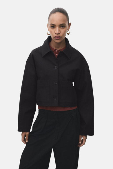 Blazer noir de MANGO, avec des manches longues et une fermeture à boutons, associé à une chemise brune et un pantalon noir.