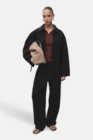 Blazer noir de MANGO, avec une coupe décontractée et porté avec un haut marron rougeâtre et des pantalons noirs larges.