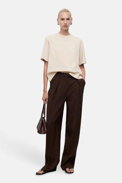 T-shirt beige à manches courtes de MANGO, modèle décontracté associé à un pantalon marron et une handte.