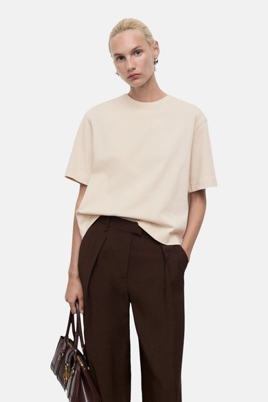 T-shirt beige à manches courtes de MANGO, porté avec un pantalon marron et une poche main bordeaux.