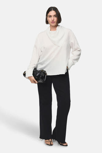 Blouse blanche à longues manches de MANGO, avec un col spécial et portée avec une jupe noire et une main.
