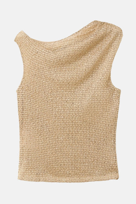 Blouse sans manches dorée de MANGO, avec une texture brillante et portée avec des boucles d'oreilles voyantes.