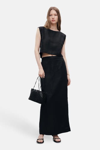 Blouse sans manches noire de MANGO, portée avec une longue jupe noire et un sac tissé.