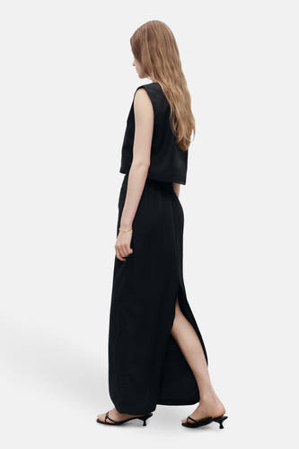 Blouse sans manches noire de MANGO, associée à une longue jupe fendue et des sandales compensées.