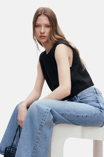 Blouse noire sans manches de MANGO, portée avec un jean à jambes larges sur une chaise blanche.