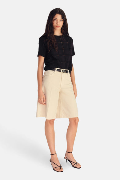 T-shirt noir à manches courtes de Mango, avec un motif perforé, associé à un pantalon beige et des sandales noires.