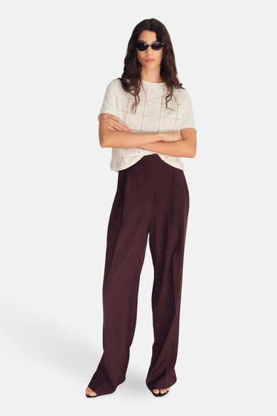 T-shirt blanc à manches courtes de MANGO, avec un motif carré, associé à des pantalons prune et un chapeau de soleil.