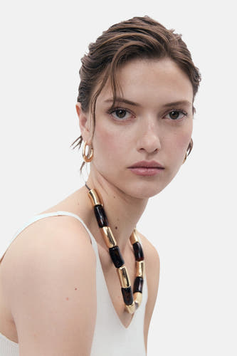 T-shirt blanc de MANGO, porté avec une chaîne voyante et des boucles d'oreilles en or.