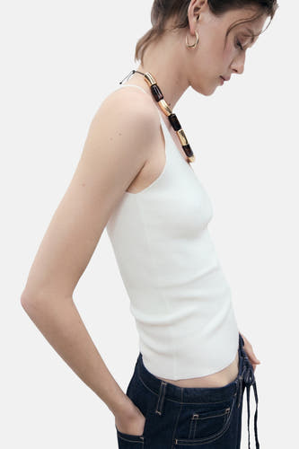 Maillot blanc de MANGO porté par un modèle tailleur avec un jeans bleu foncé et une chaîne de couleursante, vue de profil.