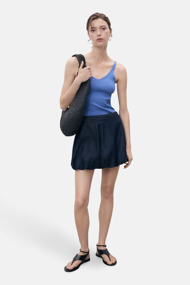 T-shirt bleu de MANGO, porté avec une courte jupe, des sandales noires et un sac tissé.