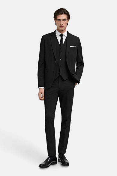 Gilet noir de MANGO, porté sous un costume noir assorti et une chemise blanche et une cravate noire.