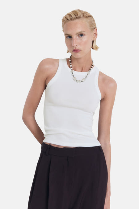 T-shirt blanc de MANGO, porté avec une chaîne de perles et un pantalon foncé.