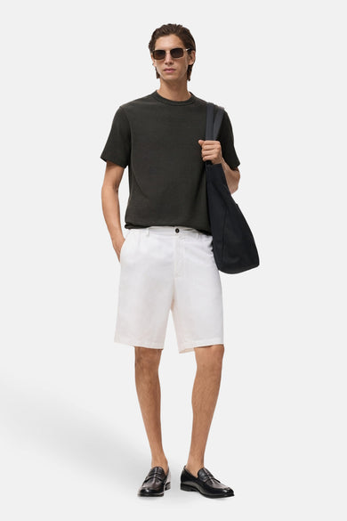 T-shirt noir à manches courtes de MANGO, porté avec des shorts blancs et des loafers noirs, avec un sac à épaules.