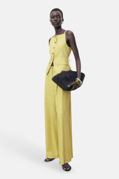Pantalon vert MANGO, avec des rayures verticales et une large ceche, associé à un gilet jaune et une sac noir.