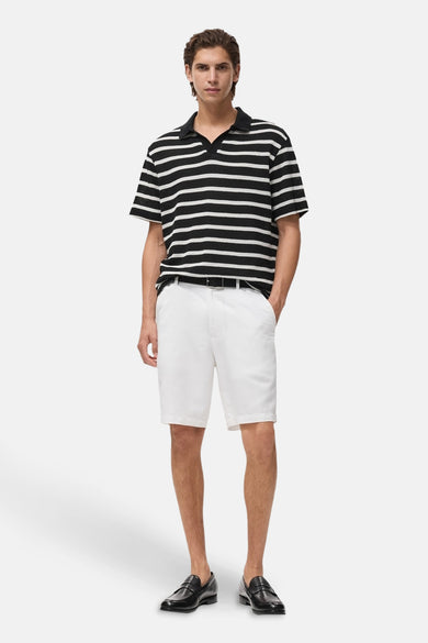 Polo rayé noir de MANGO avec des manches courtes, porté avec des shorts blancs et des loafers noirs.