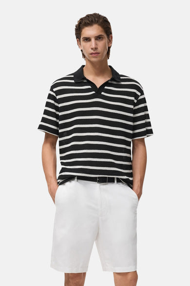T-shirt à manches courtes noir de MANGO, avec des rayures horizontales blanches, porté avec des shorts blancs et une ceinture noire.