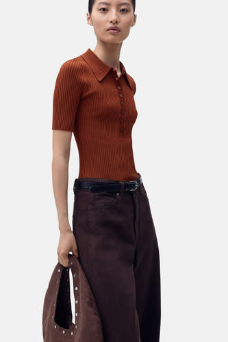 Pull marron avec col rond de MANGO, porté avec des pantalons marrons foncés à cece et une sacoche marron.