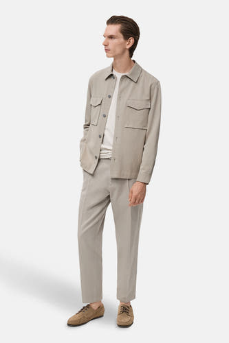 Chemise beige à longues manches de MANGO, avec des poches et portée avec un T-shirt blanc et une pantalon beige.