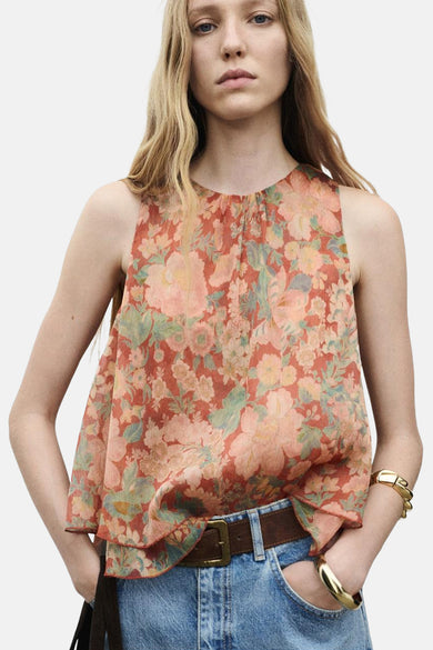 Blouse multicolore sans manches de MANGO, à imprimé fleuri, portée avec une ceinture brune et des jeans.