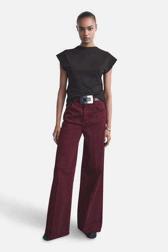 Jean de couleur bordeaux de MANGO, large et avec une ceinture à boucle argentée, associé à un t-shirt noir.