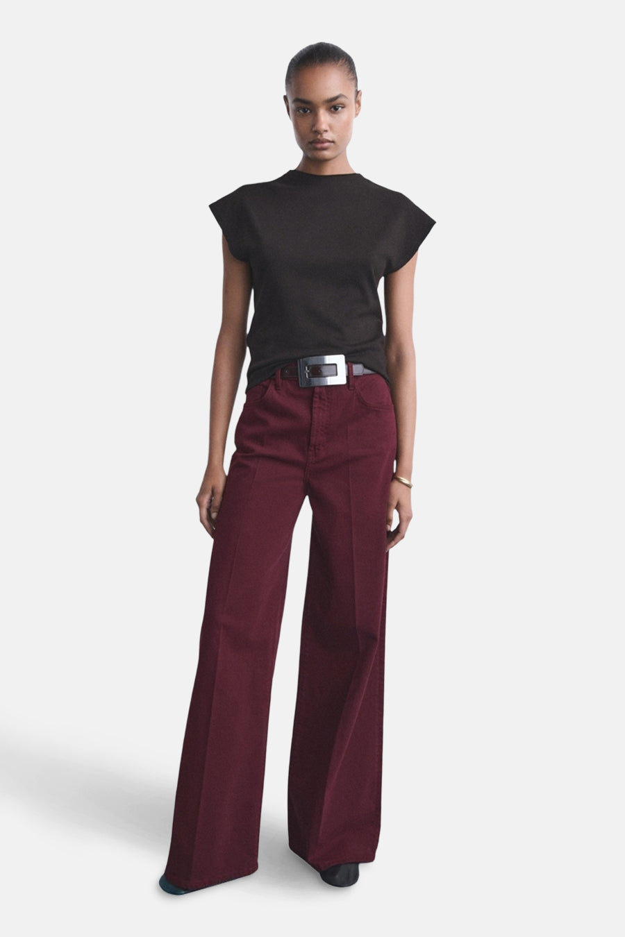 Jean de couleur bordeaux de MANGO, large et avec une ceinture à boucle argentée, associé à un t-shirt noir.