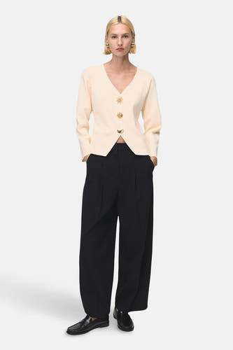 Gilet écru de MANGO, avec des boutons dorés détaillés avec des rayons de soleil, combiné à des pantalons noirs et des chaussures noires.
