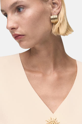 Gilet écru de MANGO, avec col V et une broche décorative dorée.