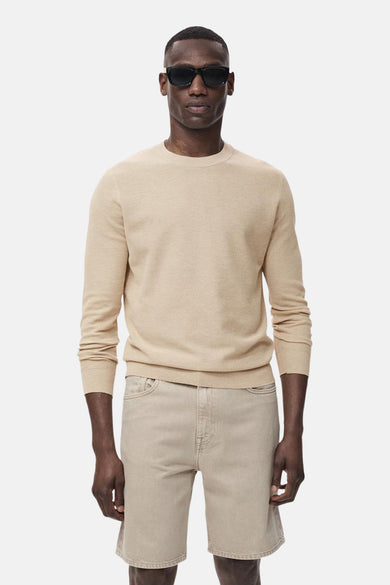 Pull beige avec col rond de MANGO, porté avec des shorts en denim et un chapeau de soleil.