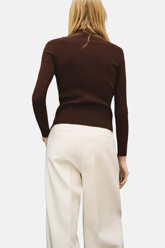 Gilet marron de MANGO, vu de de derrière, avec des manches longues et un fin tissu côtelé, associé à un pantalon crème.
