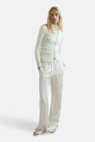 Gilet beige de MANGO, porté avec un pantalon coordonné et une chemise tricotée à manches longues.
