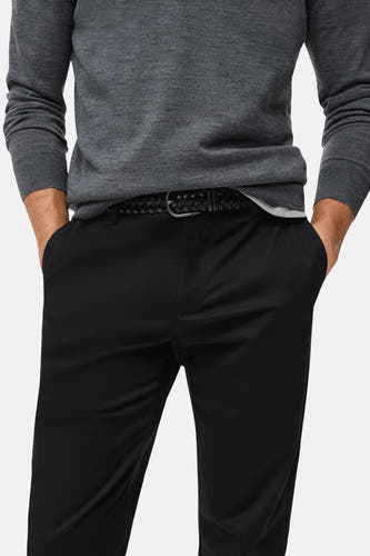 Pantalon bleu marine de MANGO, avec une ceinture tressée noire, et les mains dans les poches.