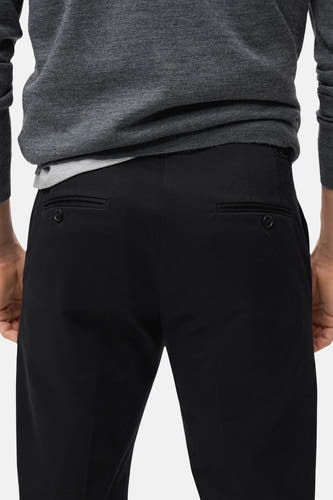 Pantalon noir de MANGO, avec des poches arrière à boutons, associé à un pull gris.