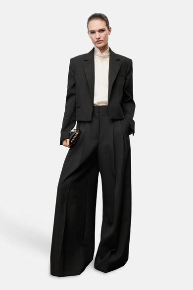 Zwarte kostuumbroek van MANGO, met wijde pijpen en gecombineerd met een crèmekleurige blouse en een korte blazer.
