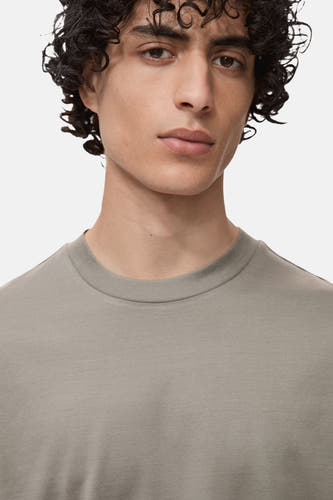 T-shirt gris à manches courtes de MANGO, gros plan du corps supérieur d'un modèle aux cheveux bouclés.