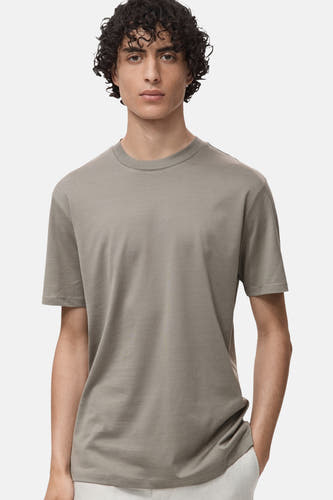 T-shirt gris à manches courtes de MANGO, porté par un modèle aux cheveux bouclés et à un pantalon blanc.