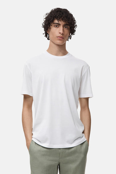 T-shirt blanc à manches courtes de MANGO, porté avec un pantalon vert et les mains dans les poches.