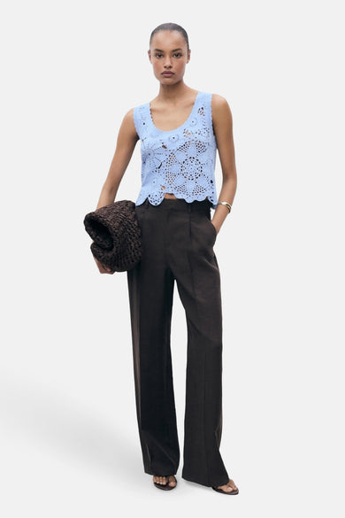 T-shirt bleu sans manches de MANGO, avec un motif de fleurs tricoté, associé à un pantalon marron et une pochette.