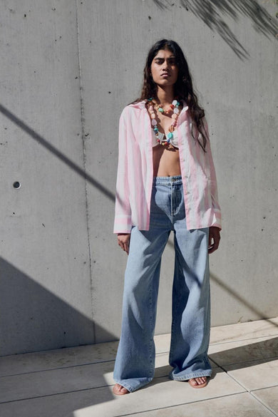 Chemise rose à manches longues de MANGO, portée avec des boutons ouverts et une chaîne colorée.