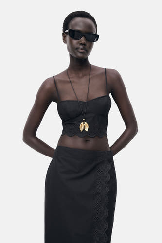 T-shirt spaghetti noir de MANGO, avec des détails de broderie anglaise le long du bas, porté avec une chaîne d'or.