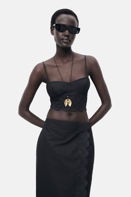 T-shirt spaghetti noir de MANGO, avec des détails de broderie anglaise le long du bas, porté avec une chaîne d'or.