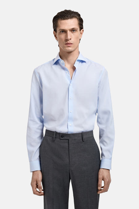 Chemise bleue à manches longues de MANGO, portée avec un pantalon gris.