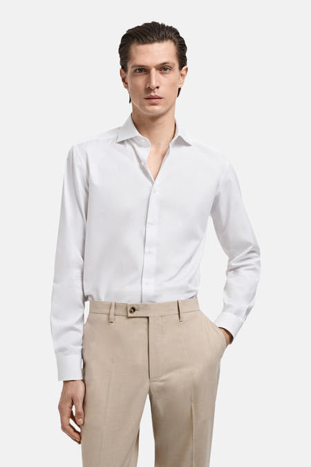 Blouse blanche à manches longues de MANGO, portée avec un pantalon beige et une main dans la poche.