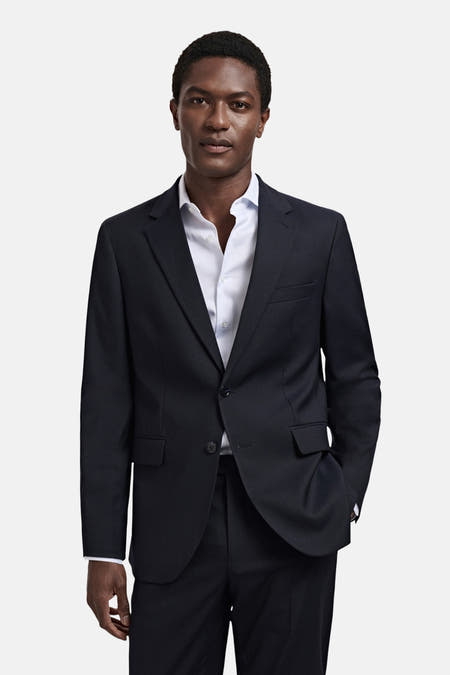 Blazer bleu de MANGO, avec un chemisier rayé bleu clair en dessous, et une main dans la poche.