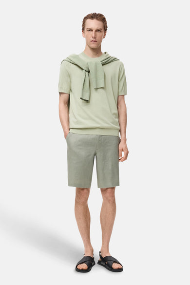 T-shirt vert avec manches courtes de MANGO, associé à un pull sur les épaules et des short gris.