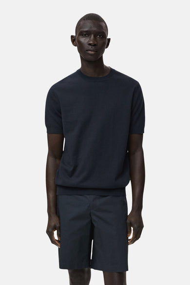 T-shirt bleu à manches courtes de MANGO, porté avec des shorts bleus marine, contre un fond blanc.
