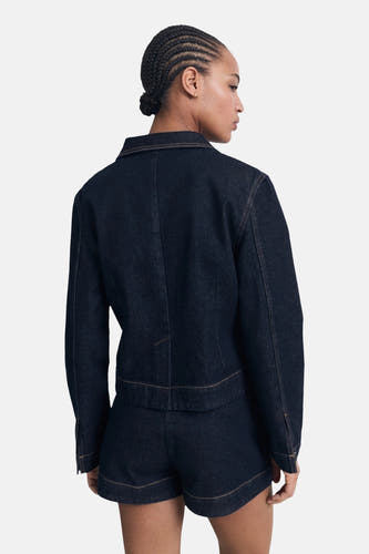 Veste en jeans bleu marine de MANGO, vue de derrière, avec des coutures contrastantes et portée avec des shorts coordonnés.