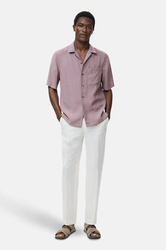 Chemise bleue à manches courtes de MANGO, avec col boutonné, poche poitrine et associée à un pantalon blanc.