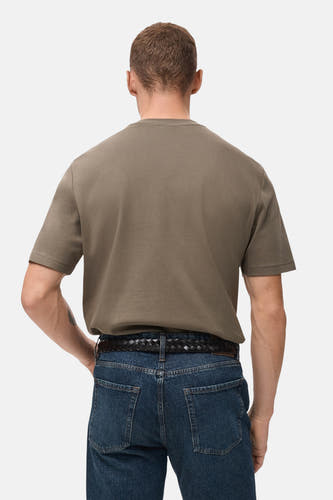 T-shirt kaki à manches courtes de MANGO, avec un col rond et porté avec une ceinture tressée et des jeans.