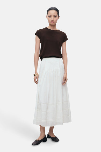 T-shirt sans manches marron de MANGO, associé à une jupe plissée blanche et des chaussures noires.