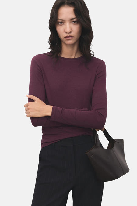 T-shirt bordeaux avec manches longues de MANGO, porté avec un pantalon rayé et une pochette en cuir.
